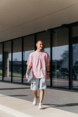 Dışarıda pembe dizüstü bilgisayarda okuyan genç bir öğrenci güzel bir havada modern bir üniversite binasında serbest çalışıyor. Yüksek kalite fotoğraf