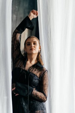 Saf siyah dantelli, kendine güvenen kadın beyaz perdeler arasında duruyor, somut güç, zarafet ve modern gotik moda. Yüksek kalite fotoğraf