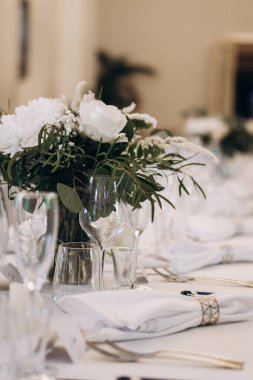 Sofistike bir kutlama için beyaz çiçekler, cam örtüler ve katlanmış peçetelerle süslenmiş zarif bir düğün yemeği masası. Yüksek kalite fotoğraf