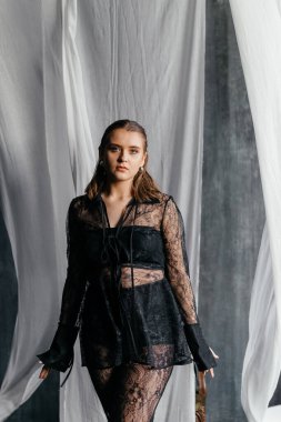 Saf siyah dantelli, kendine güvenen kadın beyaz perdeler arasında duruyor, somut güç, zarafet ve modern gotik moda. Yüksek kalite fotoğraf