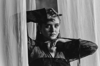 Saf siyah dantelli, kendine güvenen kadın beyaz perdeler arasında duruyor, somut güç, zarafet ve modern gotik moda. Yüksek kalite fotoğraf