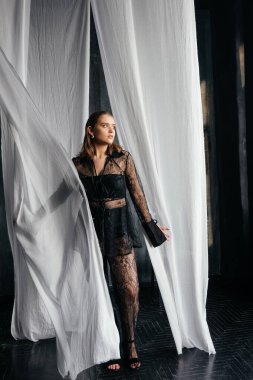 Saf siyah dantelli, kendine güvenen kadın beyaz perdeler arasında duruyor, somut güç, zarafet ve modern gotik moda. Yüksek kalite fotoğraf