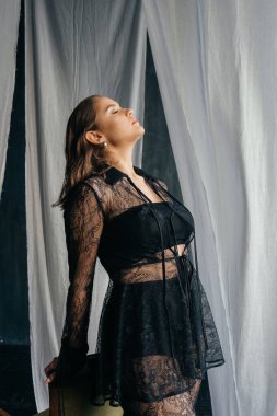 Saf siyah dantelli, kendine güvenen kadın beyaz perdeler arasında duruyor, somut güç, zarafet ve modern gotik moda. Yüksek kalite fotoğraf