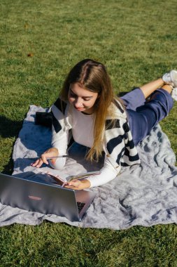 Öğrenci kız yazın dışarıda çalışıyor. Holliday 'de yeşil çimlerin üzerinde dizüstü bilgisayar kullanıyor ve not alıyor.