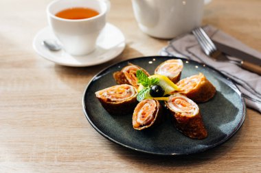 Rolls of thin pancakes with smoked salmon and cream cheese on dark plate on wooden table. Delicious and healthy breakfast or brunch