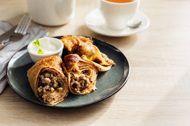 Crepes stuffed with chicken and mushrooms with sour cream and cup of tea on the wooden table