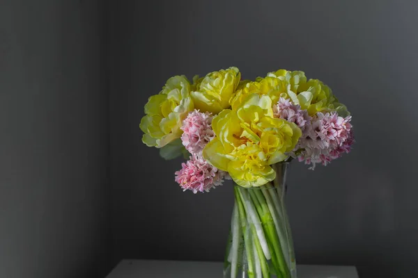 stock image Beautiful spring flower arrangement of yellow peony tulips and pink hyacinth in the glass vase.