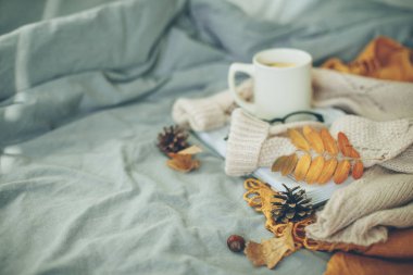 Sıcak ev atmosferi. Sıcak bej kazak, çay, kahve, kitap, gözlük ve portakal yapraklı kupa. Hygge konsepti.