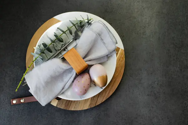 复活节快乐假期的概念 深色背景桌子上的大理石盘 餐具和桉树枝条的平面图片 免版税图库图片