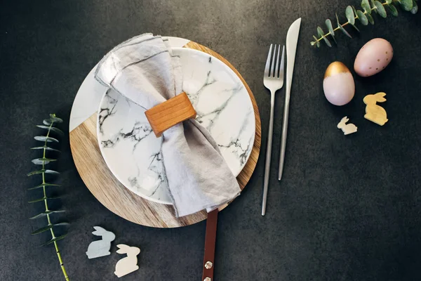 复活节餐桌设置的概念 在深色的背景桌子上 有盘子 复活节蛋 餐具和桉树枝条 平躺在地上 俯瞰四周 图库图片