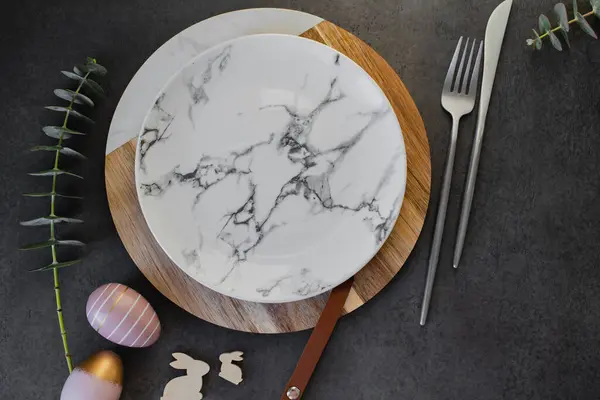 复活节餐桌设置的概念 深色背景桌上的盘子 复活节蛋 餐具和桉树枝条 图库照片