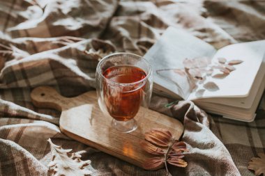 Atmosferik fotoğraf, açık bir kitap, bir fincan çay ve yatakta sonbahar yaprakları. Boşluğu kopyala