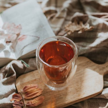 Evdeki sıcak sonbahar mevsimi. Bardakta sıcak çay, açık kitap ve sonbahar yaprakları..