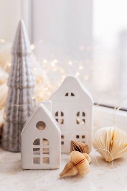 Yeni yıl iç dekorasyonları. Beyaz dekoratif seramik evler, Noel ağacı, çelenk ışıkları, arka planda süslü kağıtlar. Noel sıcacık kışlık ev dekorasyonu.