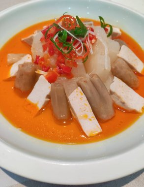 Baharatlı buğulanmış tofu ve soğumuş sebzeler beyaz tabakta kırmızı yağda.