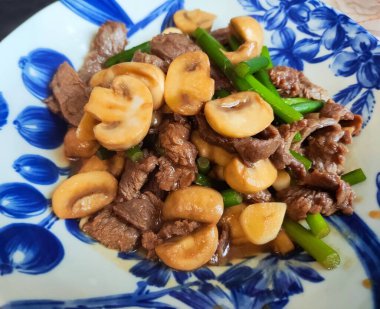 Mavi tabakta sığır eti ve yeşil sebzelerle karıştırılmış mantarlar.