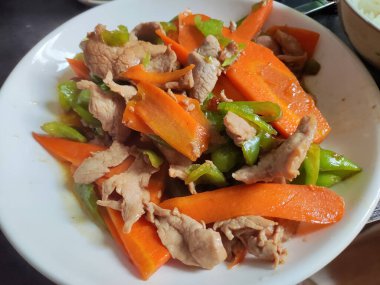 Et ve yeşil biberle karıştırılmış havuç dilimi beyaz tabakta.