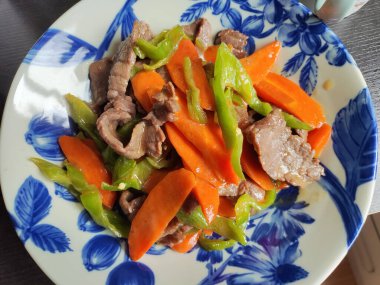 Mavi tabakta bir dilim havuç ve yeşil biberle çırpılmış domuz eti.