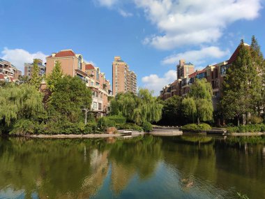 Güneşli bir öğleden sonra gölün ve ağaçların ortasındaki binaların manzarası.