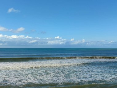 Beyaz deniz dalgaları mavi deniz suyunda güneşli bir günde mavi gökyüzünün altında akar.
