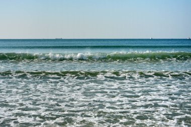 Güneşli bir günde mavi denizde beyaz dalgalar ve köpükler uçuşur.