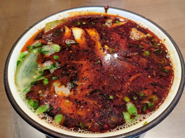 Erişte çorbasının üzerinde parlak ışık altında kırmızı biber yağı yüzüyor.