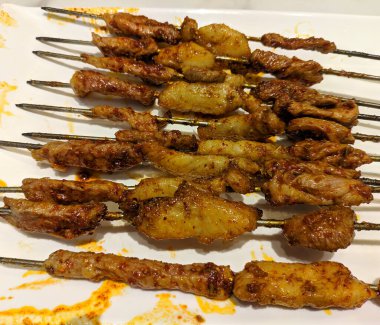 Parlak ışık altında beyaz tabakta kırmızı biberli koyun şiş kebap
