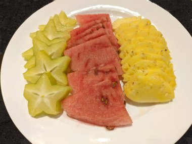 Taze kırmızı karpuz, sarı ananas ve beyaz tabakta yemek için yeşil karambola.