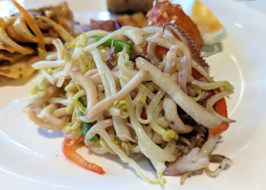 Parlak ışık altında, beyaz tabakta sebzeli kalamarı karıştır.