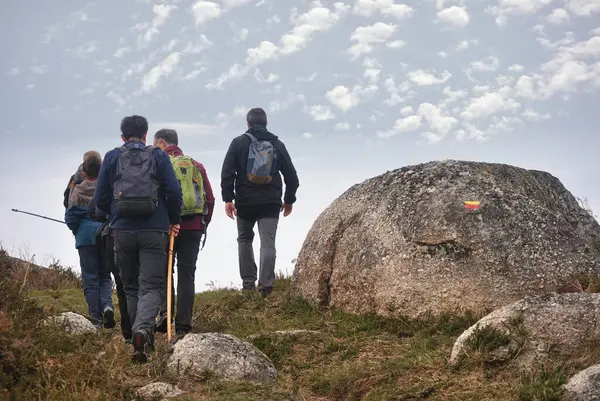 Bir grup insan bir patikada dağa tırmanıyor, spor, keşif, yol işaretleri bir taşın üzerine kazınmış.