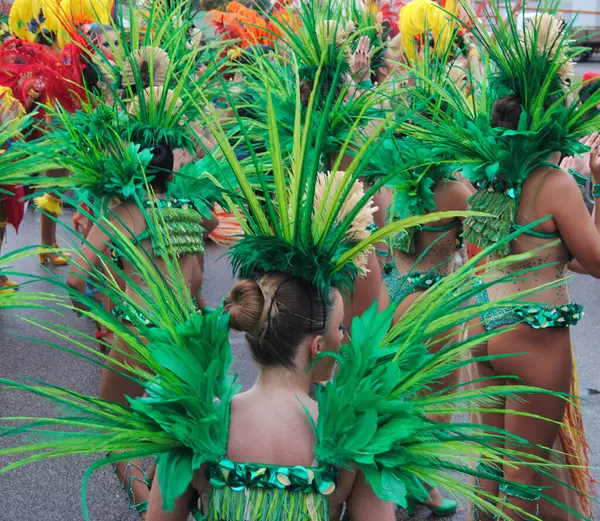 Yağmurlu ve soğuk bir günde yeşil, kırmızı ve sarı renklerle sokak geçidinde süslü kostümlü, tüylü ve bikinili bir grup dansçı.