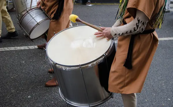 Yağmurlu bir günde sokağın ortasında davul grubu bas davul çalan müzisyenlerle gösteri yapıyor.