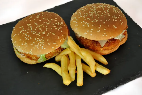 Kızarmış patatesli iki hamburger, tahtada servis ediliyor, yemeye hazır.