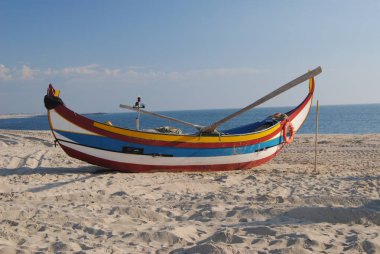 Küçük bir balıkçı teknesi kumsalda durdu. Zengin sarı, mavi ve kırmızı boya işi, beyaz arka plan.