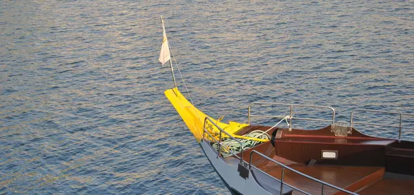Sarı pruva, sarı uçlu ve bayraklı bir teknenin önünde, arkada nehir suyu var.