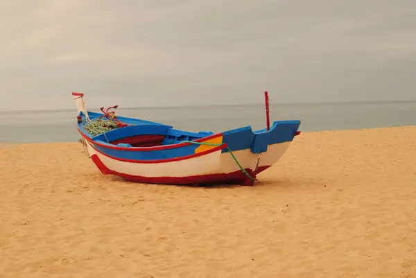 Sahilde yalnız bir tekne, arkasında ufukta beliren beyaz, mavi ve kırmızı renklerle kumsalda durdu.