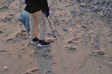 Plajda elinde torbayla çöpleri toplayan bir adam, çevrenin temizlenmesine yardımcı olmak için beton plastikler.