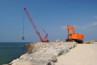 Turna, vinç ve bir kazıcı deniz kenarı için kırmızı ve turuncu bir şantiye