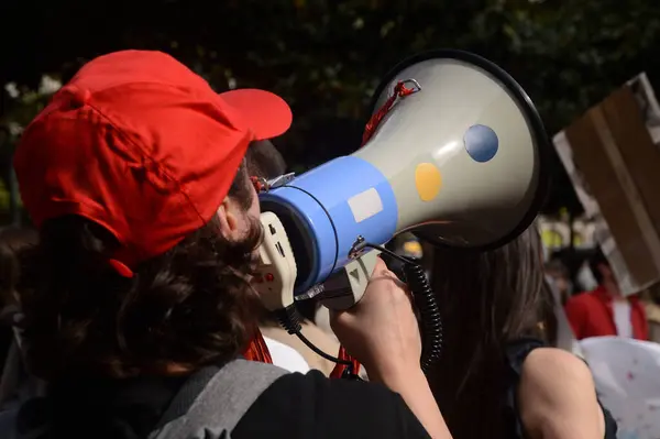 Protesto için kırmızı şapkalı bir kişi megafona doğru konuşuyor.