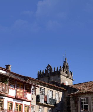 Portekiz 'in Guimares şehrindeki eski bir meydanda ortaçağ saat kulesi, Oliveira Leydimizin Kilisesi, eski binaların ön cephesi, balkonlarda kuruyan giysiler, tipik