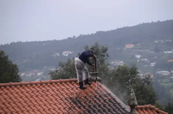 Yağmurlu bir günde dağın tepesindeki kilisenin çatısını yıkayan bir adam.