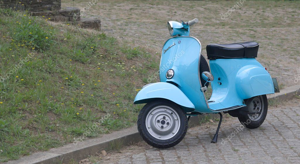 Light blue motorbike parked on a street in an old village, scooter, Italian made, classic model from the 60s, next to a garden with flowers