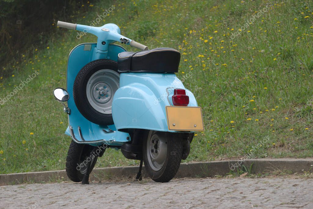 Old blue Italian motorcycle parked next to a garden with flowers