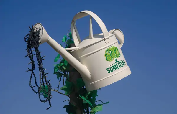 El yapımı reklam paneli, eski sulama tenekesi yapay bitki süslemeleri olan bir çubuğa asılmış, nadir bulunan ve basılmış logodan çıkan içeceği taklit eden ışık dizileri.