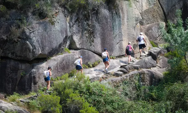 Bir grup insan bir dağ yamacına tırmanıyor, bir kayayı geçiyor.