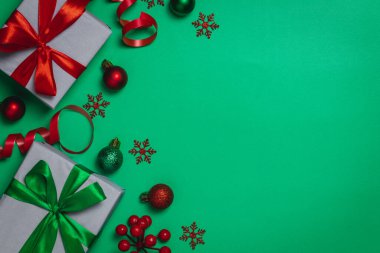 Noel arkaplanı hediye paketi, kırmızı kurdele ve yeşil arka planda Noel topları.