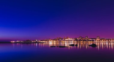 Şehir ışıkları arka planda mor alacakaranlık gökyüzü ile Douro nehrine yansıyarak güzel ve sakin bir şehir manzarası yaratıyor. Porto, Afurada 'dan uzak, Vila Nova de Gaia.