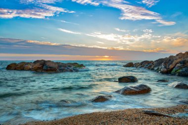 Yumuşak güneş ışığı sakin bir okyanus sahnesini yıkıyor, ön planda kayaları ve kumlu bir sahili aydınlatıyor, günbatımında sakin ve resimli bir kıyı manzarası yaratıyor. Konum: Vila Nova de Gaia, Porto, Portekiz