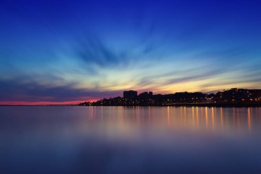 Porto, Portekiz 'deki Douro nehrinin üzerinde renkli bir gün batımı. Şehir ışıkları sakin suyu yansıtıyor ve büyülü bir atmosfer yaratıyor.