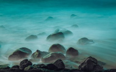 Alacakaranlıkta uzun bir pozlama sırasında sahildeki kayaların üzerinde süzülen okyanus dalgalarının hayali, ruhani bir görüntüsü sisli, dünyevi bir etki yaratıyor. Konum: Vila Nova de Gaia, Porto, Portekiz